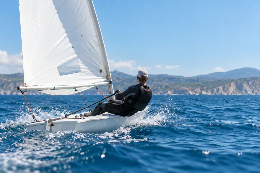 Illustrative photograph of a dinghy sailor racing on blue water
